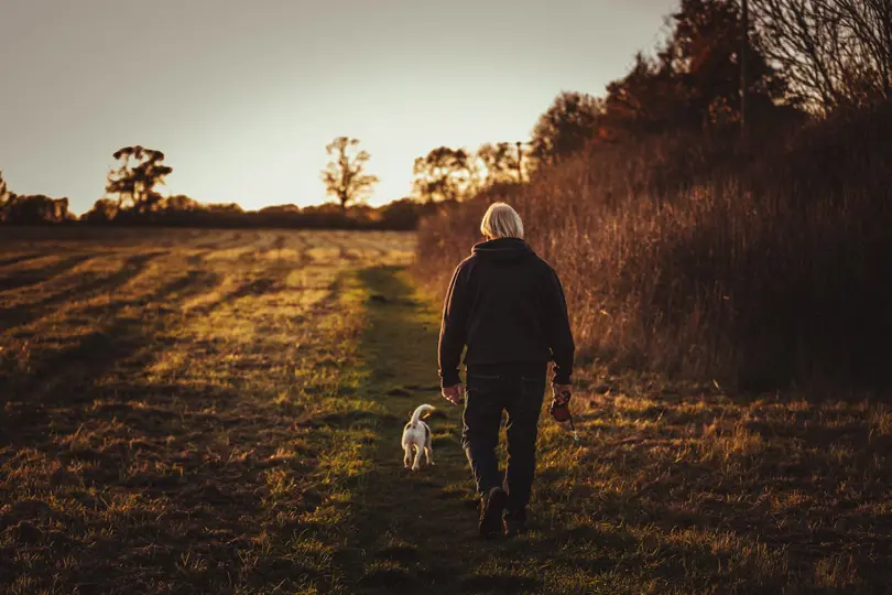 Older man walking on a field with a dog.jpg