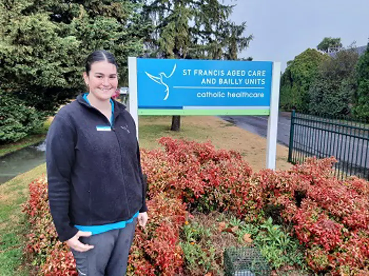 Smiling young lady standing in front of the Catholic Healthcare building signage