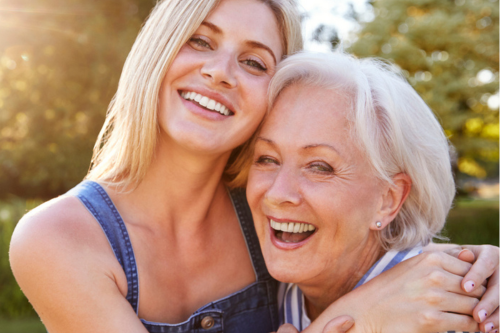 A joyful mother and daughter share a warm embrace outside in the sunshine, symbolising the comfort and independence that comes with receiving supportive home care while staying connected with loved ones.