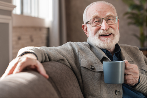 A smiling senior man enjoys a moment of comfort and relaxation in a cosy living space, reflecting the warmth, familiarity, and security offered by residential aged care.