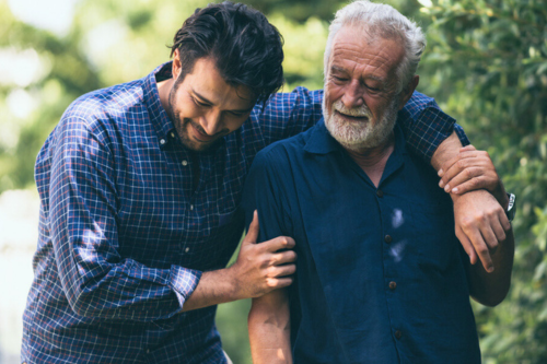 A cheerful moment between a younger man and an older gentleman as they walk together outdoors, representing the sense of companionship and community in retirement living environments.