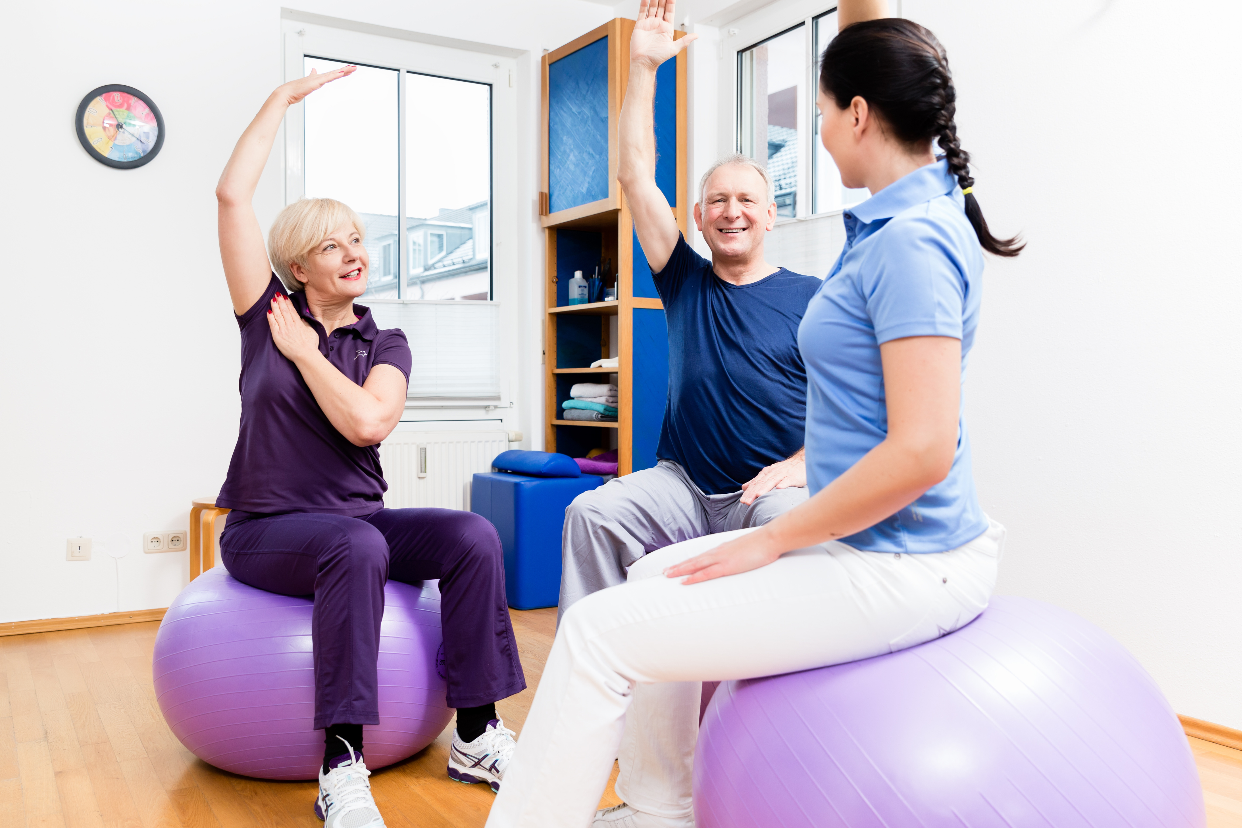 A care professional guides two senior women through strength and balance exercises using fitness balls, promoting mobility, confidence, and physical independence.