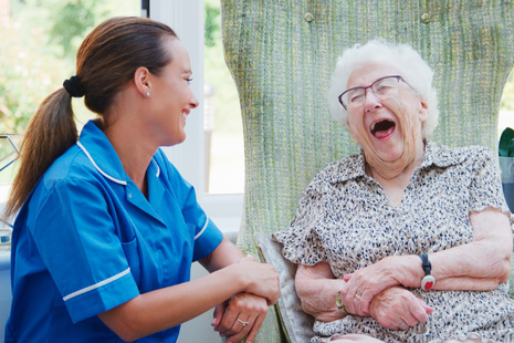 A caregiver and an elderly woman share a joyful moment, laughing together &mdash; conveying warmth, companionship, and emotional connection.
