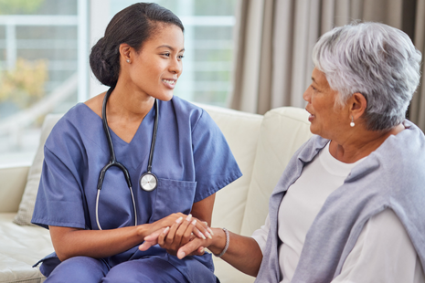 A healthcare professional, wearing scrubs and a stethoscope, holds an elderly woman&rsquo;s hands in a reassuring way, symbolising trust, empathy, and personalised medical care.