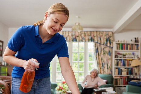a young woman wearing a blue polo shirt, cleaning a surface with a spray bottle and cloth.